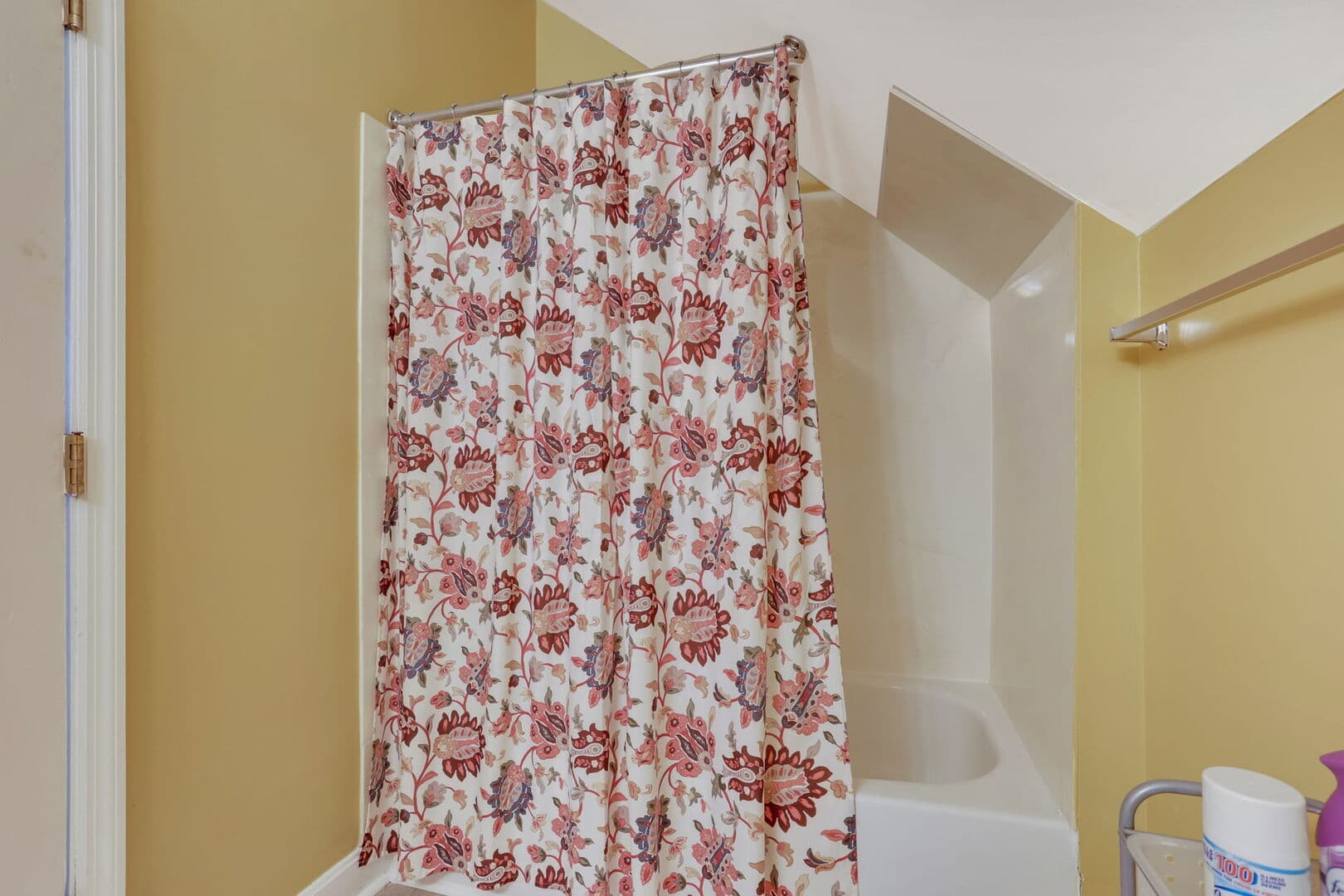 A bright bathroom with golden walls, a shower/tub combo with a red and white floral curtain, and a wall-mounted towel bar.