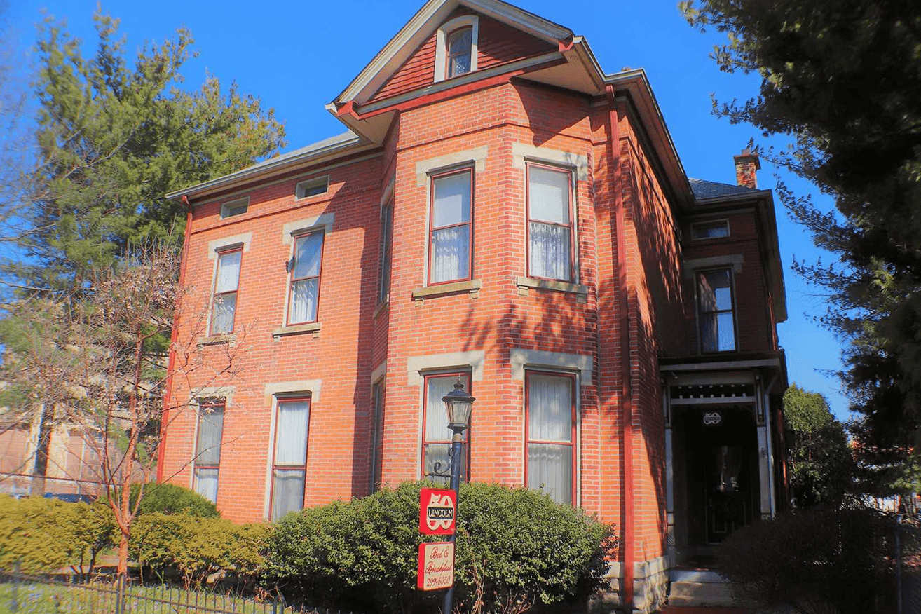 A large, historic brick house surrounded by greenery and trees.