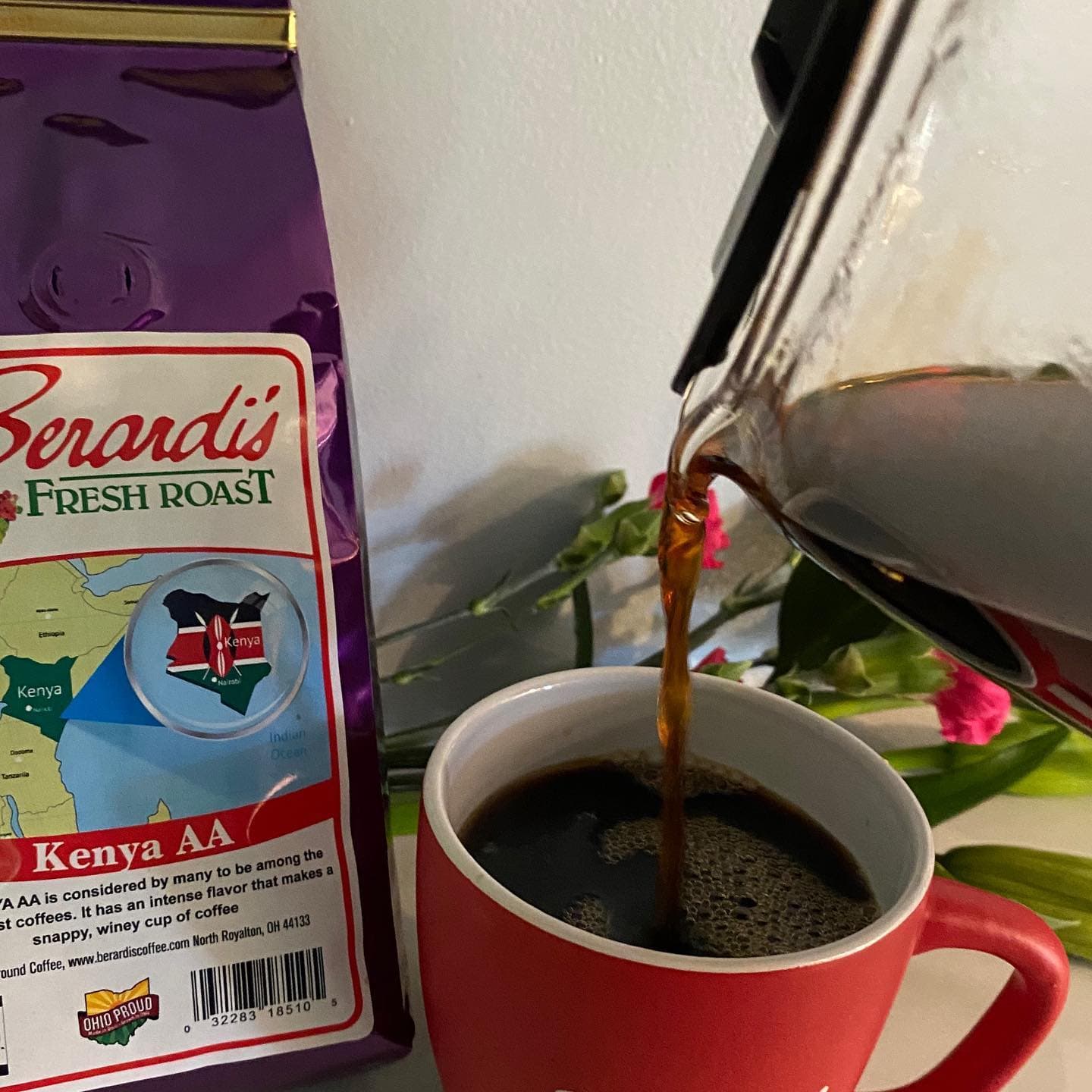 A cup of coffee being poured from a glass carafe next to a bag of Berardi's Kenya AA coffee.