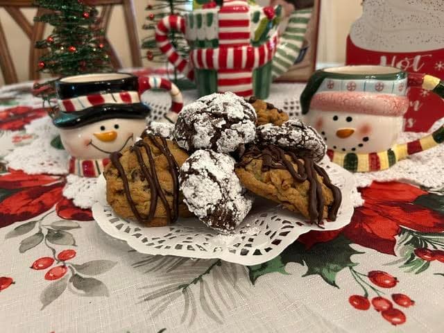 A plate of assorted cookies sits on a festive tablecloth, surrounded by decorative snowman mugs and holiday decor.