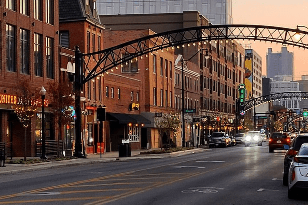 A busy street in the Short North district at twilight featuring traffic and historic storefronts under an archway.