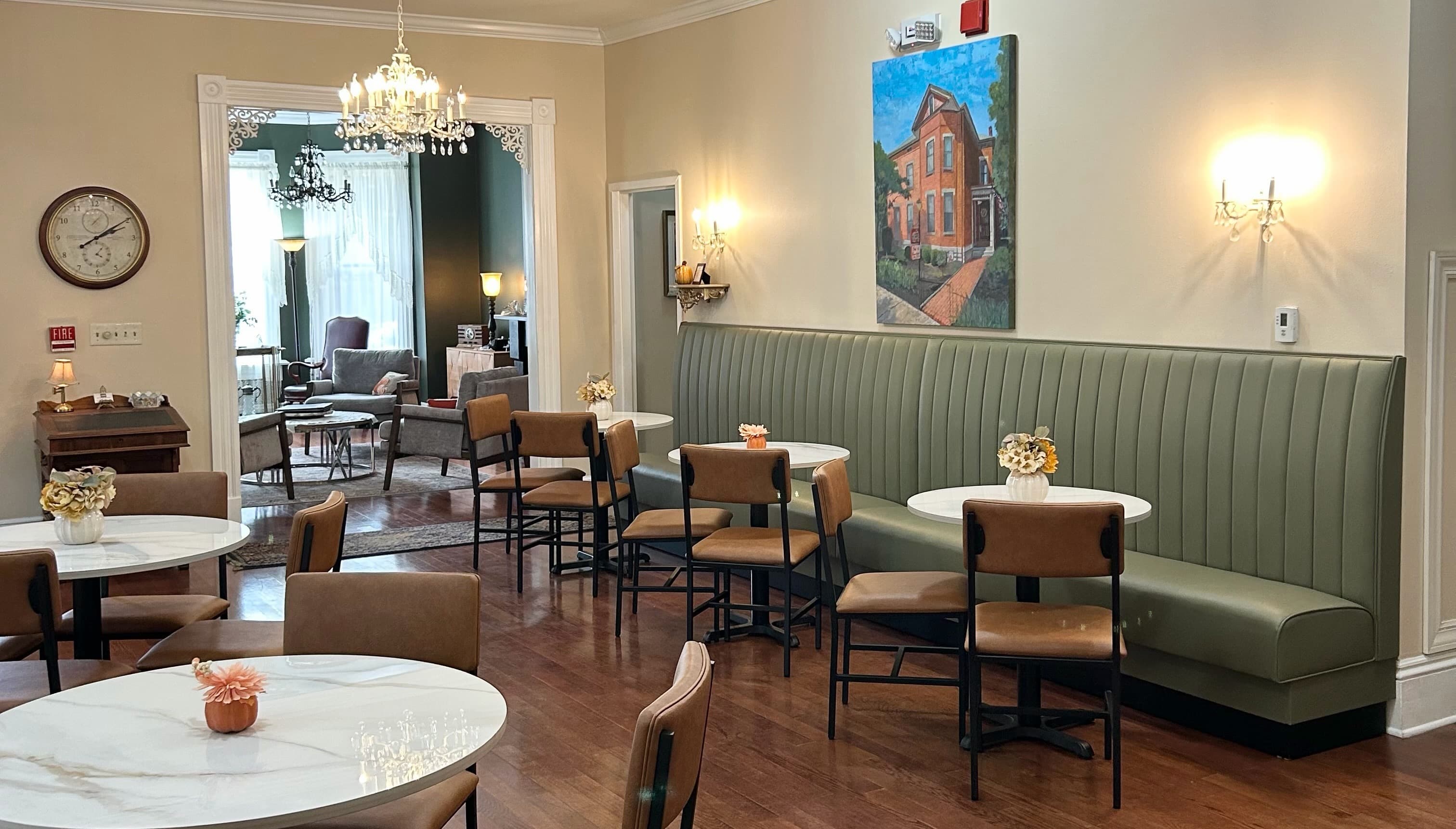 A stylish café with marble tables, green banquette seating, and artwork on the wall, featuring soft lighting and a cozy atmosphere.