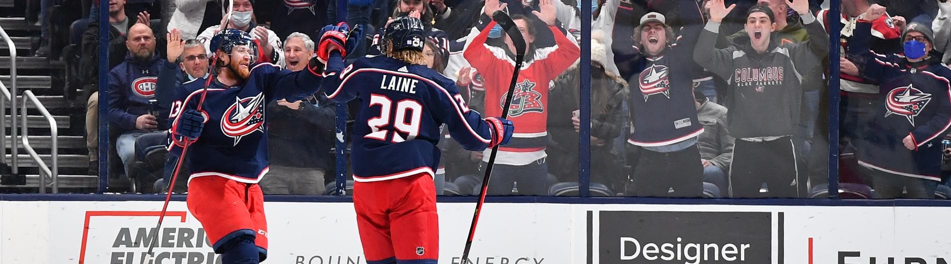 Columbus Blue Jackets players celebrate a goal as excited fans cheer in the background.