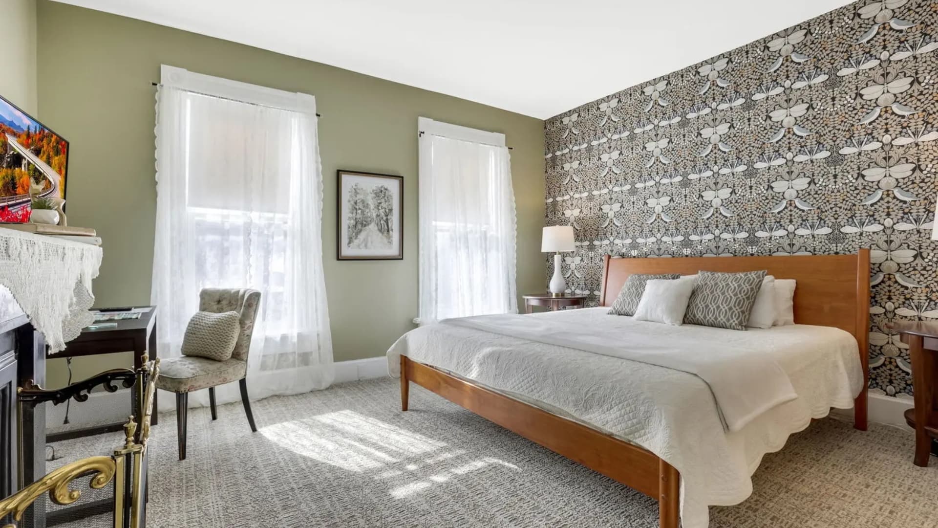Cozy bedroom featuring a wooden bed, patterned wallpaper, and large windows with natural light.