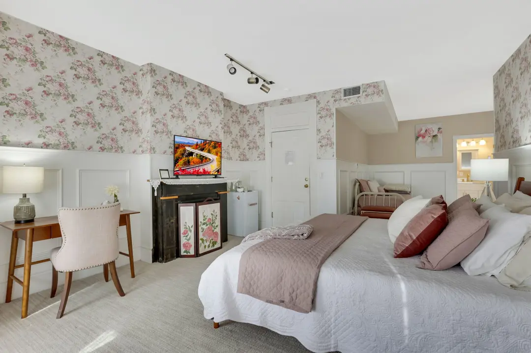 Cozy bedroom with floral wallpaper, a queen bed, a desk, and a TV.