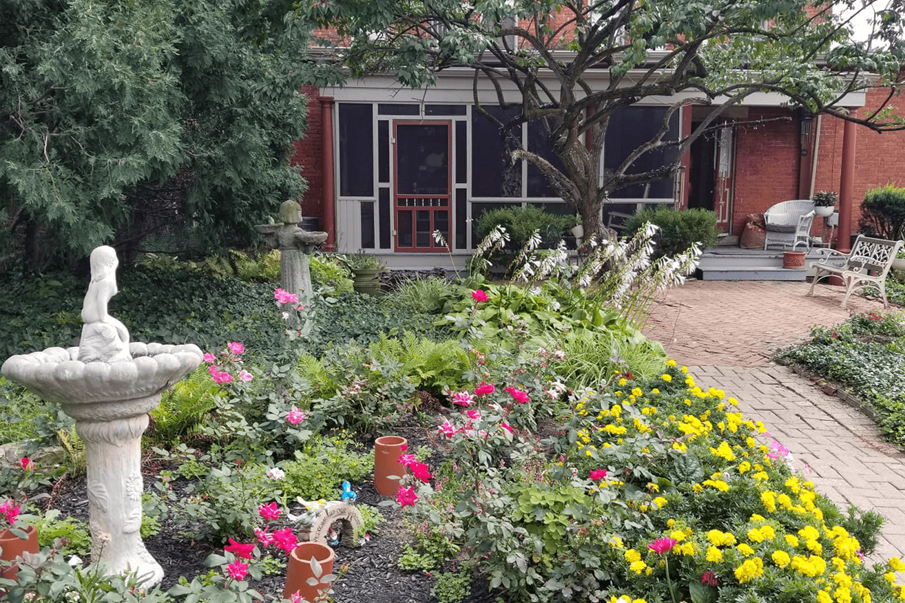 A lush garden with colorful flowers and a stone fountain, leading to a screened porch.